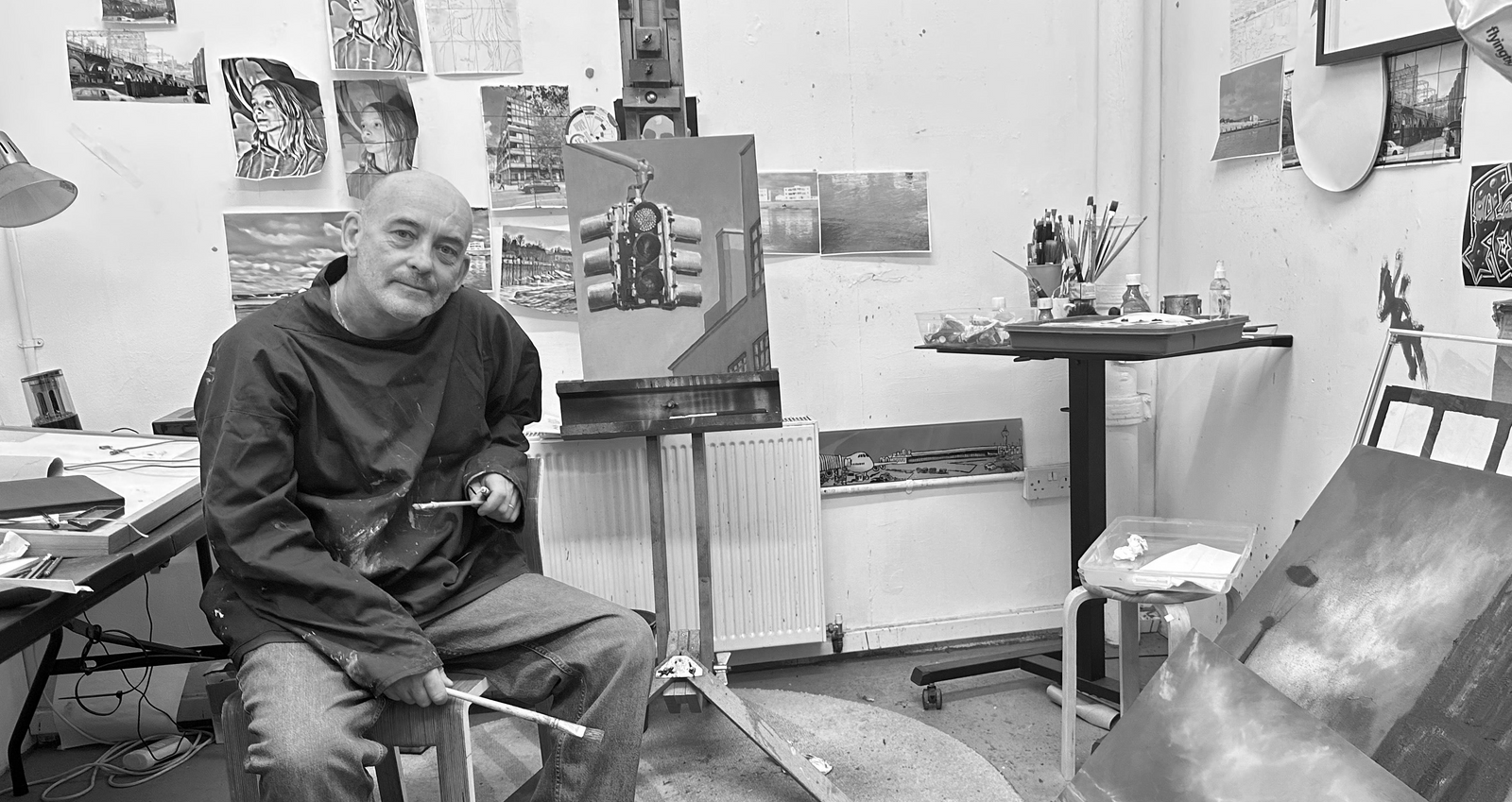 Michael Epton sitting in his art studio with art supplies and paintings on the wall.